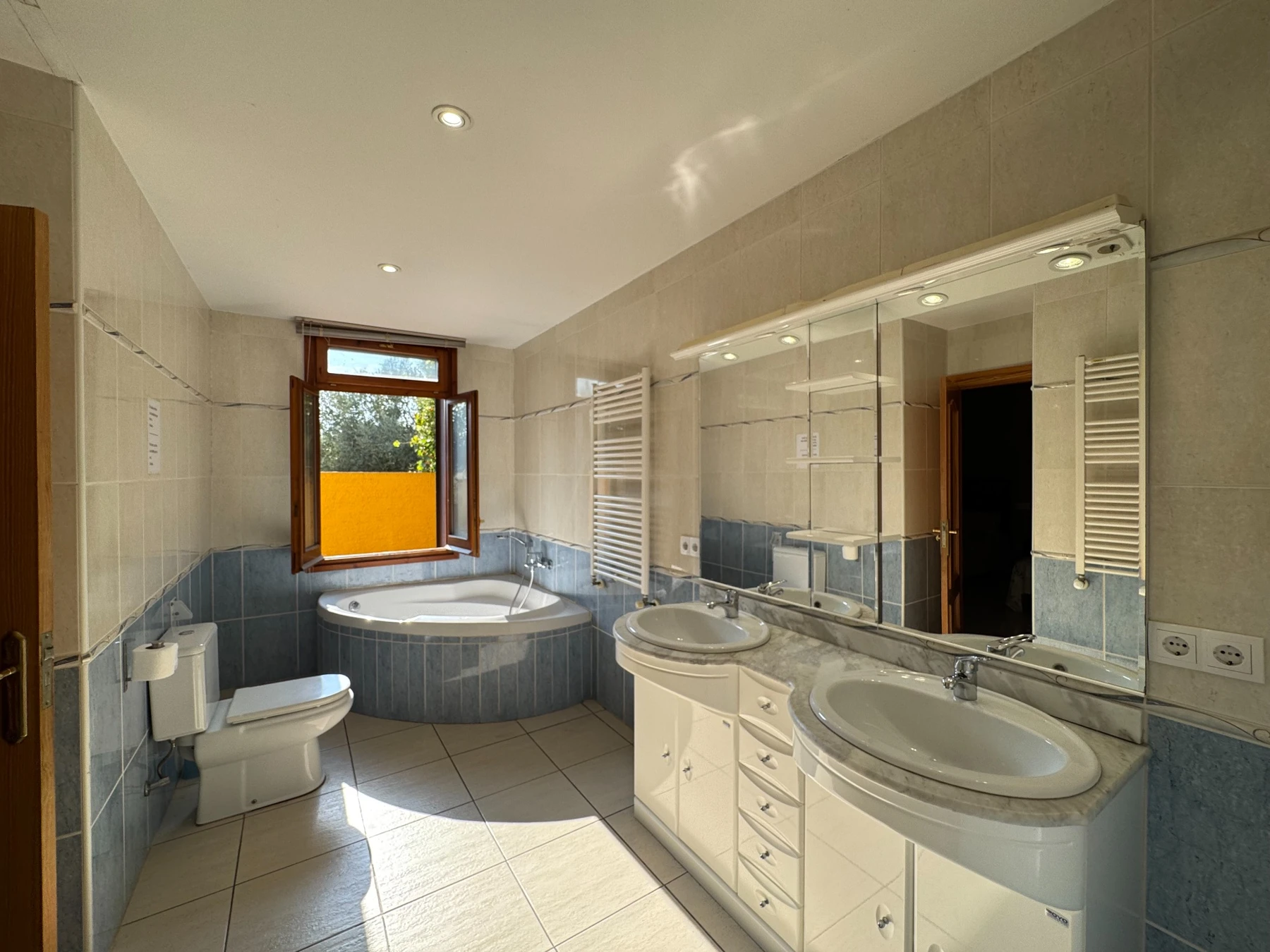 Baño con bañera esquinera, doble lavabo y ventana