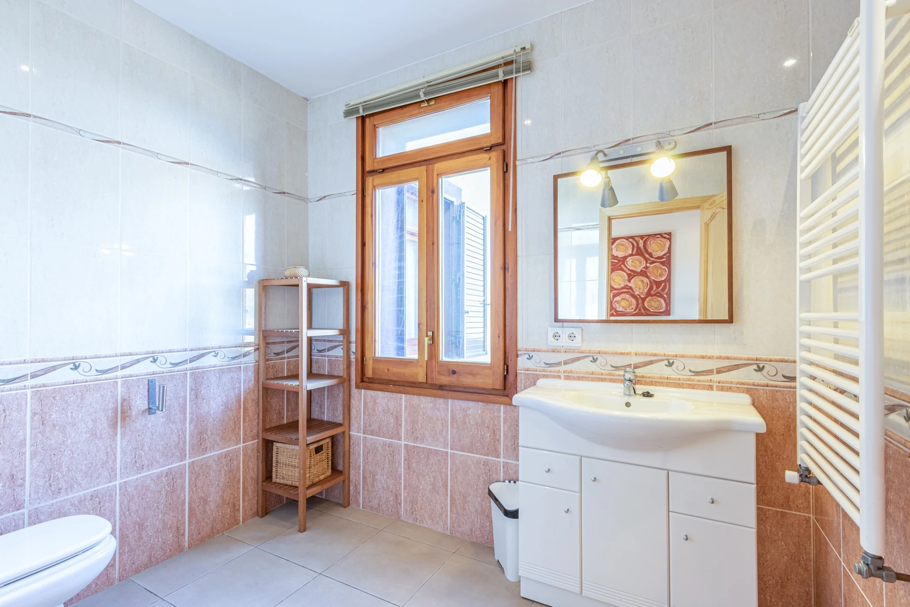 Baño con azulejos rosados, lavabo y ventana de madera