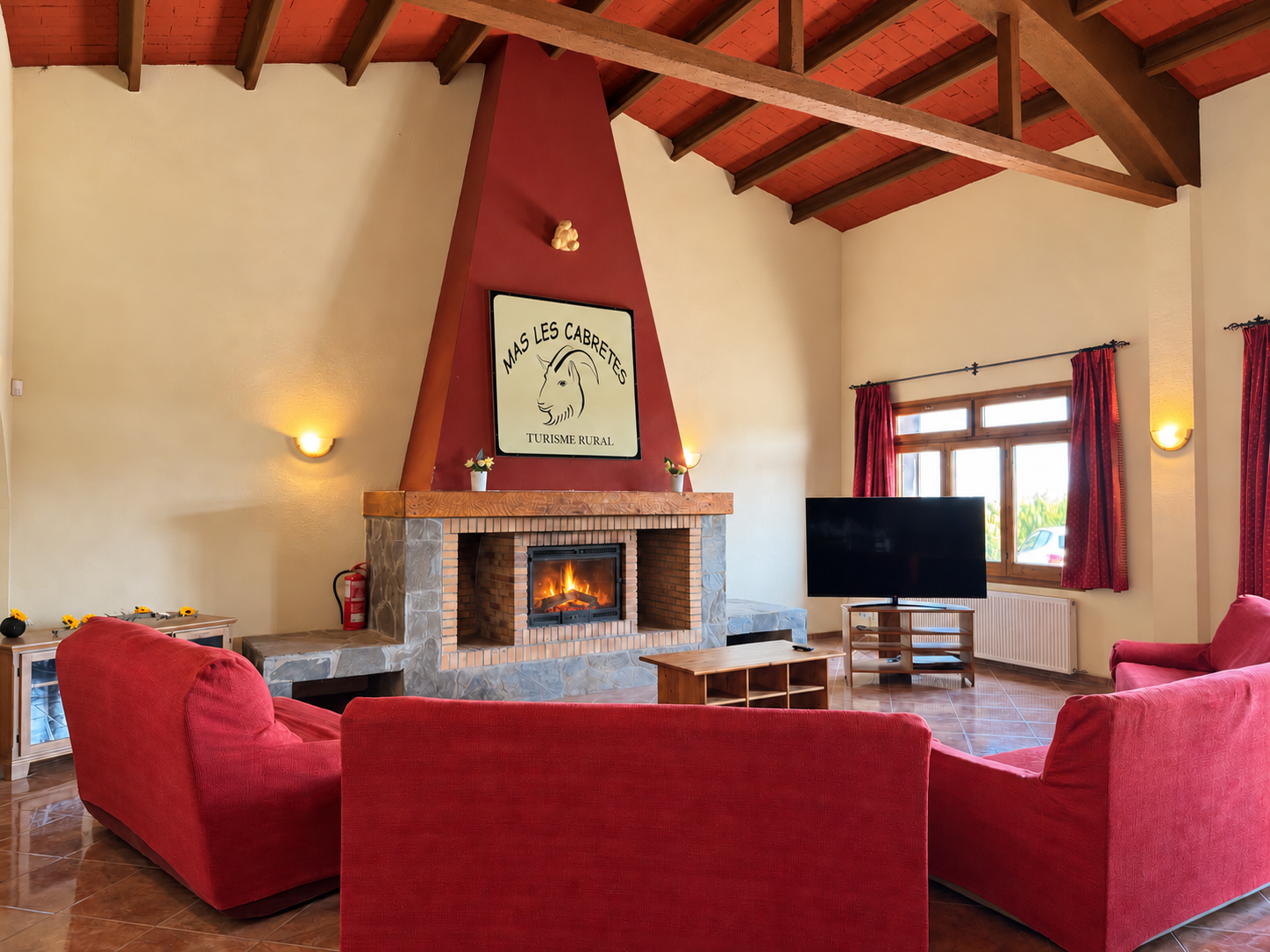 Zona de estar con sofás rojos, televisión y chimenea encendida